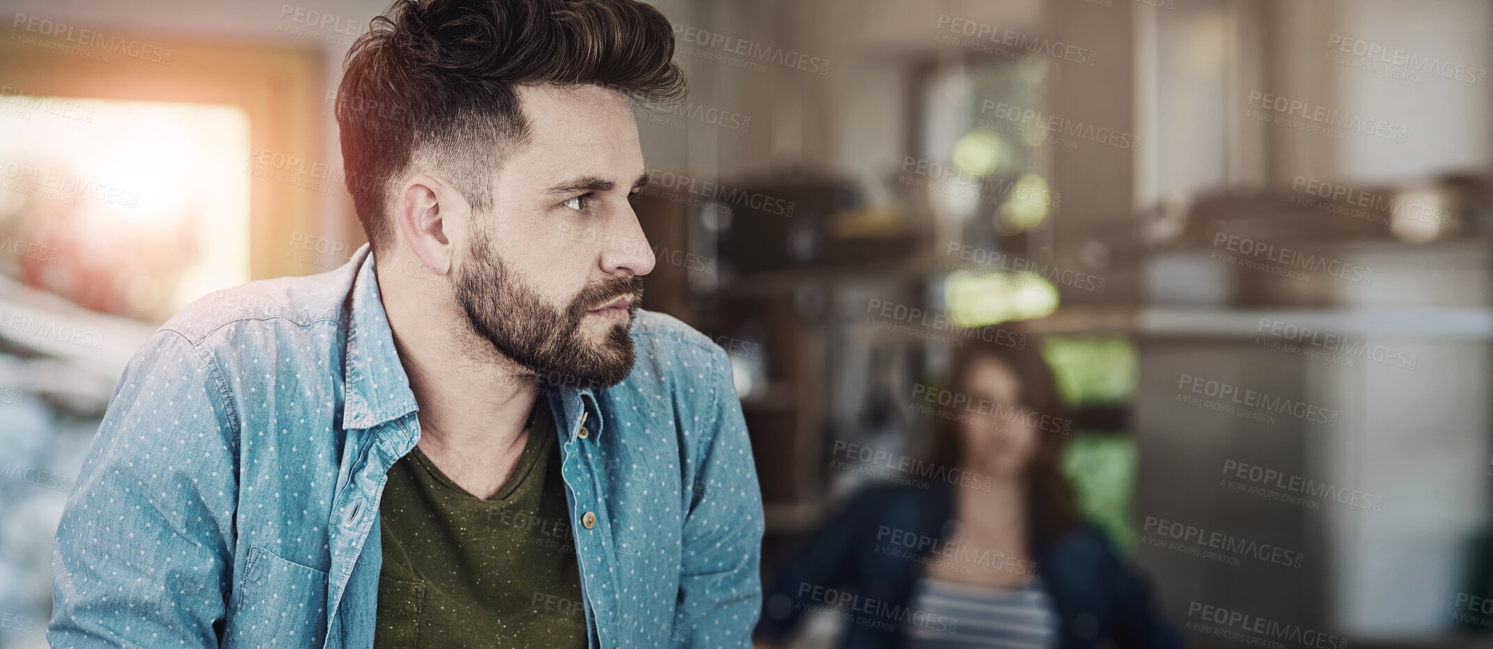 Buy stock photo Shot of a young man looking upset after a fight with his wife who is standing in the background