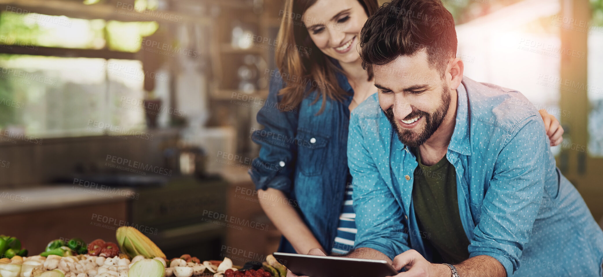 Buy stock photo Shot of a happy young couple using a digital tablet while preparing a healthy meal together at home