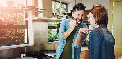 Buy stock photo Shot of a man giving his wife a taste of the food that he’s preparing at home