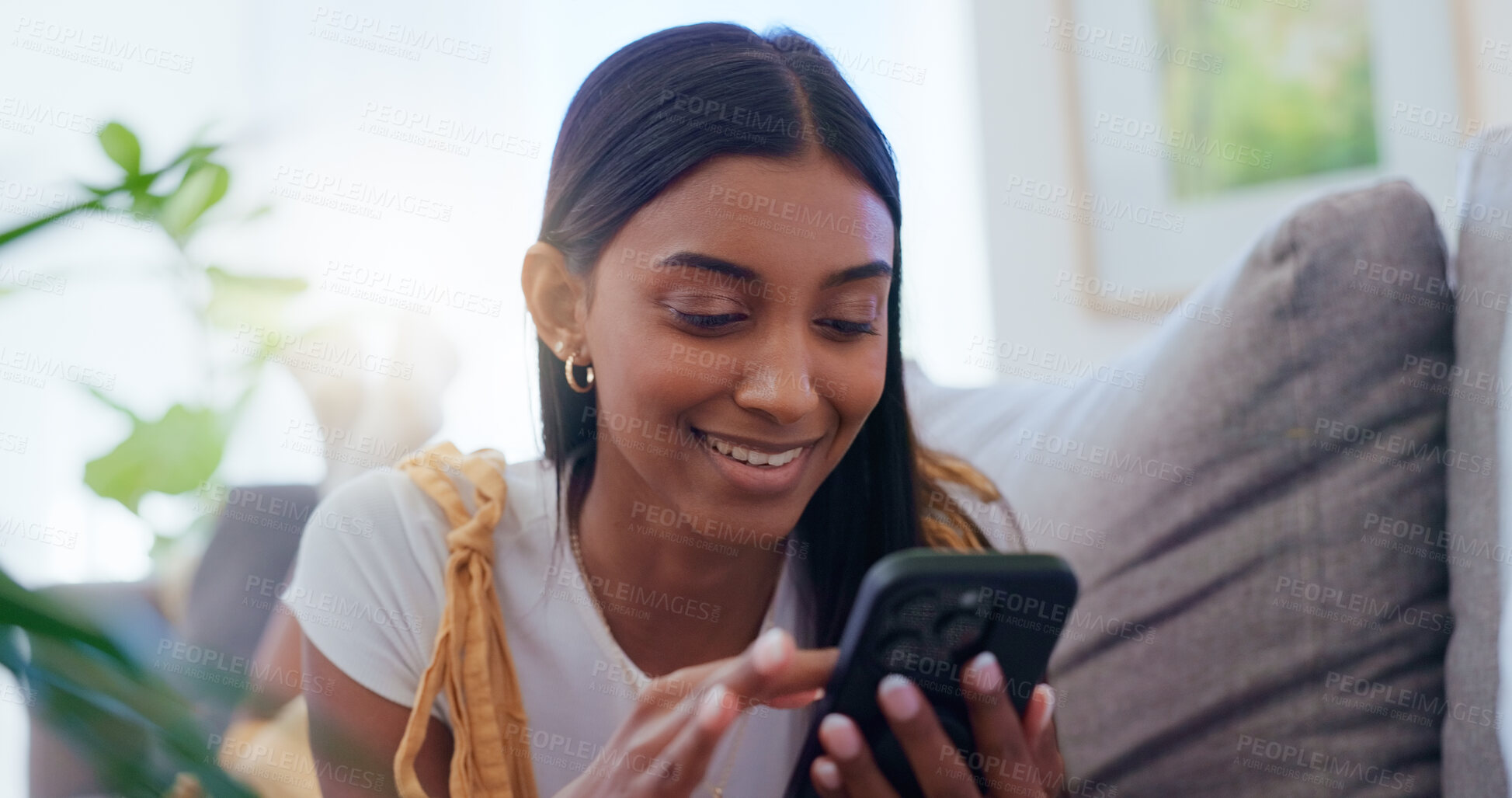 Buy stock photo Girl, sofa and smartphone with scroll in home for social media browsing, reading ebook and smile for text message. Indian woman, person and happy with phone on couch for relax or comment on blog post