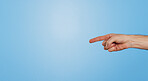 Finger, point and arm of person in studio for information, direction and announcement of news. Hand, gesture and emoji by mockup space for review, answer and feedback of opinion on blue background