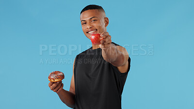 Buy stock photo Man, donut and apple in studio for health, nutrition and wellness with choice, vitamin C and versus. Male person, portrait and fruit on blue background for food, decision and weight loss with detox