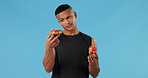 Man, donut and apple for health, choice and wellness with nutrition, vitamin C and versus in studio. Male person, portrait and fruit on blue background for food, decision and weight loss with detox