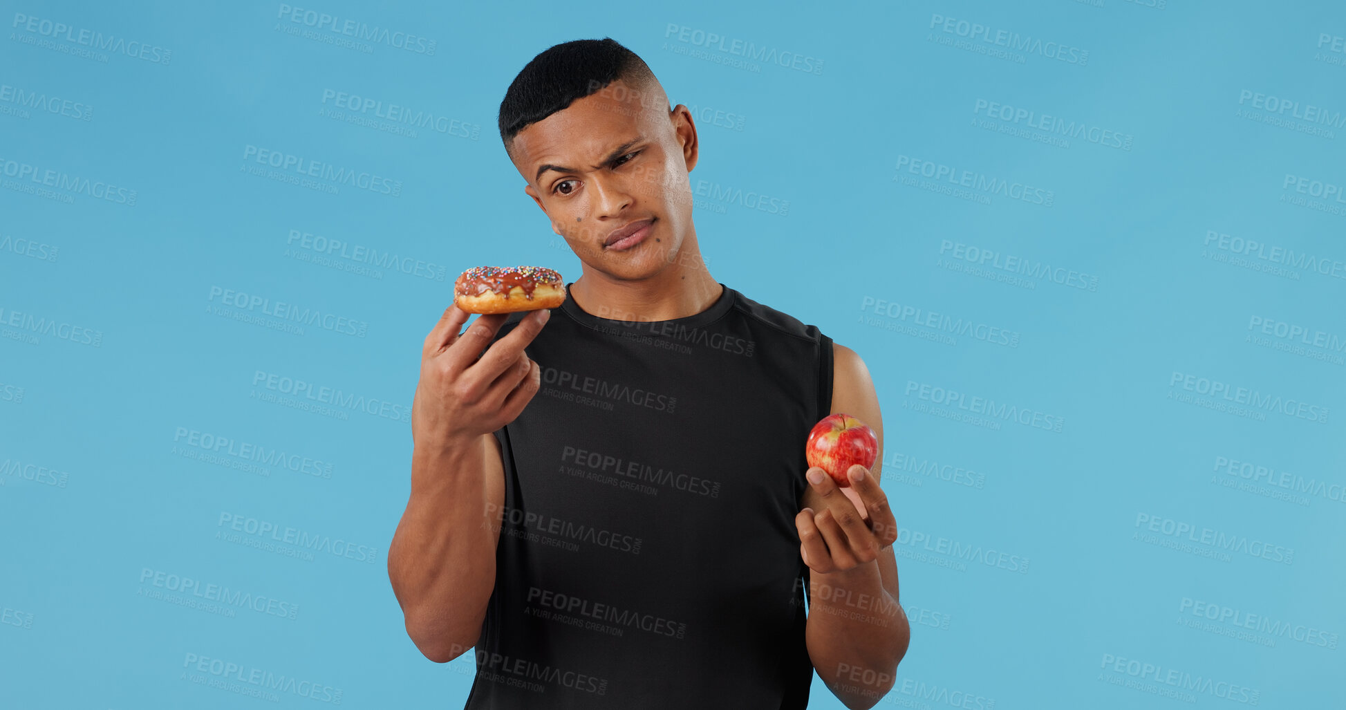 Buy stock photo Man, donut and apple for health, choice and wellness with nutrition, vitamin C and versus in studio. Male person, portrait and fruit on blue background for food, decision and weight loss with detox