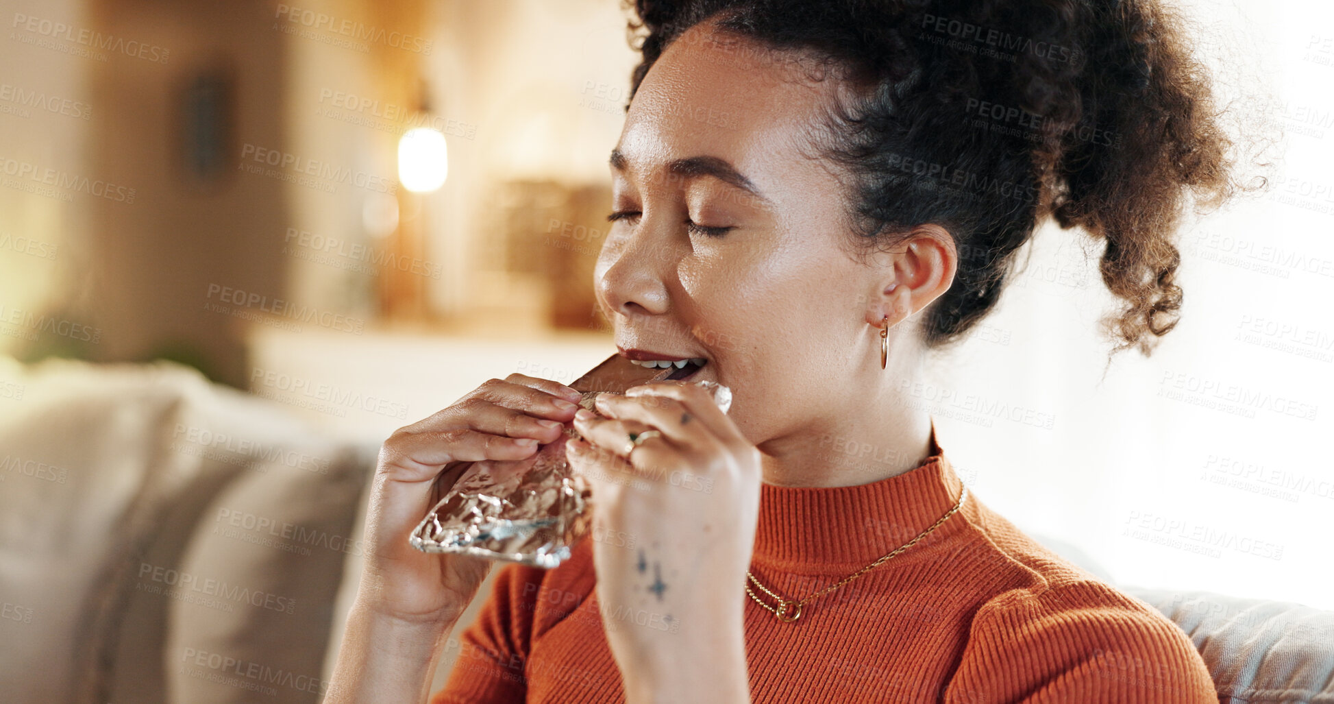 Buy stock photo Break, chocolate and face of woman on sofa in living room of home to relax for weekend wellness. Candy, eating and food with happy African person in apartment for satisfaction or sweet indulgence