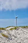 Wind turbine, blue sky and beach with sand for renewable energy, alternative power or natural sustainability in nature. Empty, fan or eco friendly environment with resource, generator or green supply