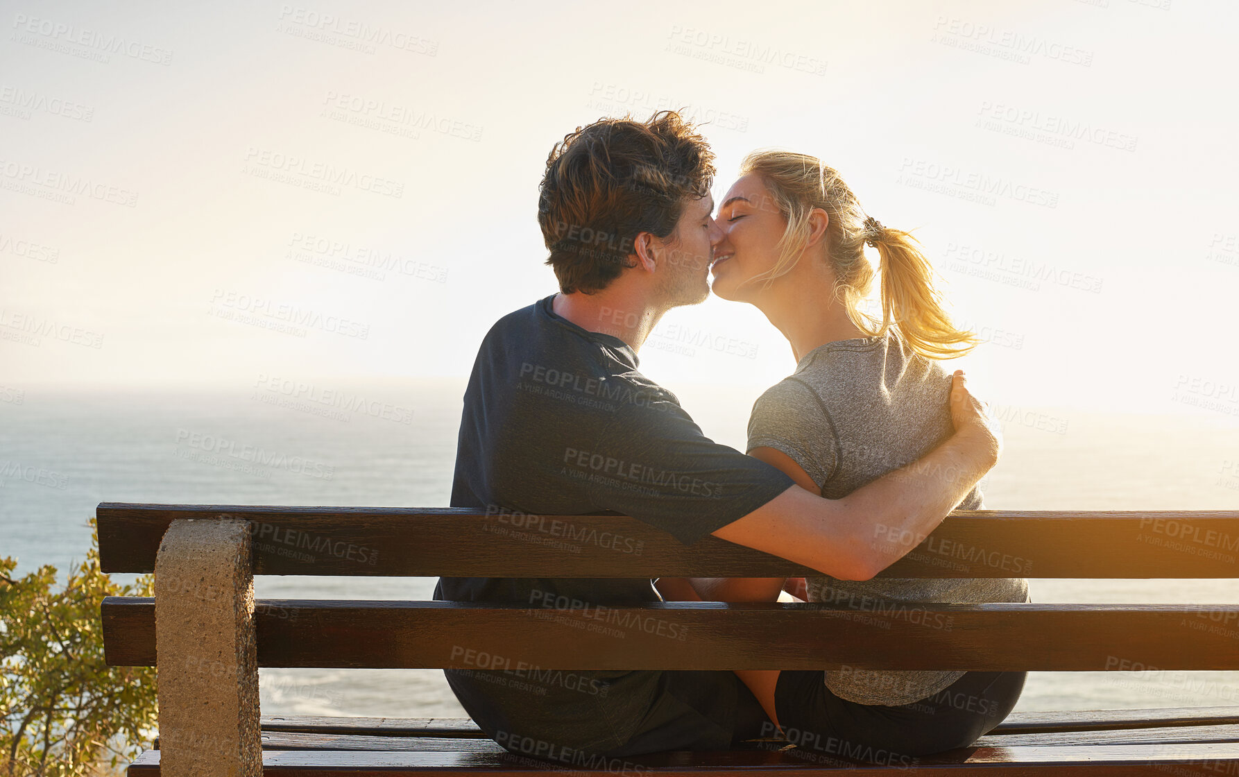 Buy stock photo Love, kiss and couple at sea at sunset for date, hug or bonding together on bench on holiday. Happy, man and woman at ocean for romantic relationship, support and connection with partner on vacation