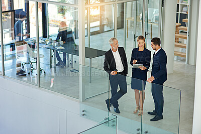 Buy stock photo Shot of three colleagues talking together over a digital tablet while standing in a modern office