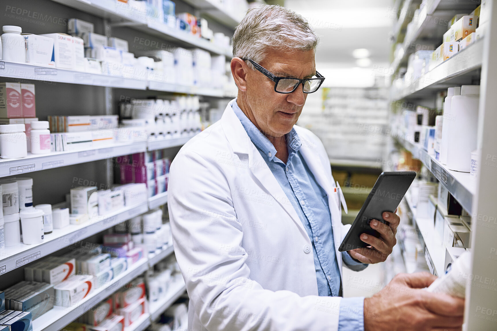 Buy stock photo Shot of a focused mature male pharmacist making notes of the medication stock on the shelves in a pharmacy