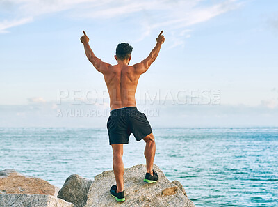 Buy stock photo Fitness, man and freedom with celebration on rocks at beach for workout success training achievement. Athlete back, shirtless and hands up at ocean for exercise progress, body goals and run victory