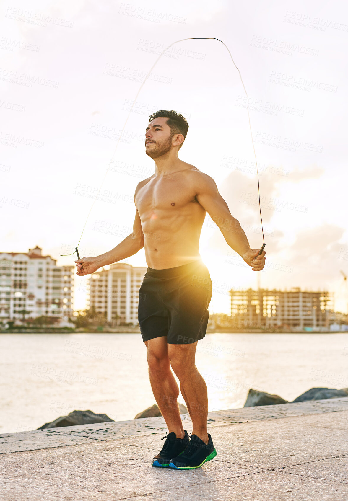 Buy stock photo Man, skipping and fitness by beach for body, exercise and muscle development with sunshine by sea. Athletic, workout and topless outdoor for training, endurance and jump rope with cardio activity