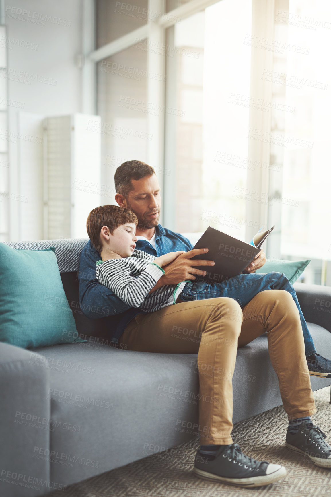 Buy stock photo Home, reading book and dad with boy on sofa, relax and bonding together in living room. Apartment, family and single parent on couch, son and kid with storytelling, childhood and father in lounge