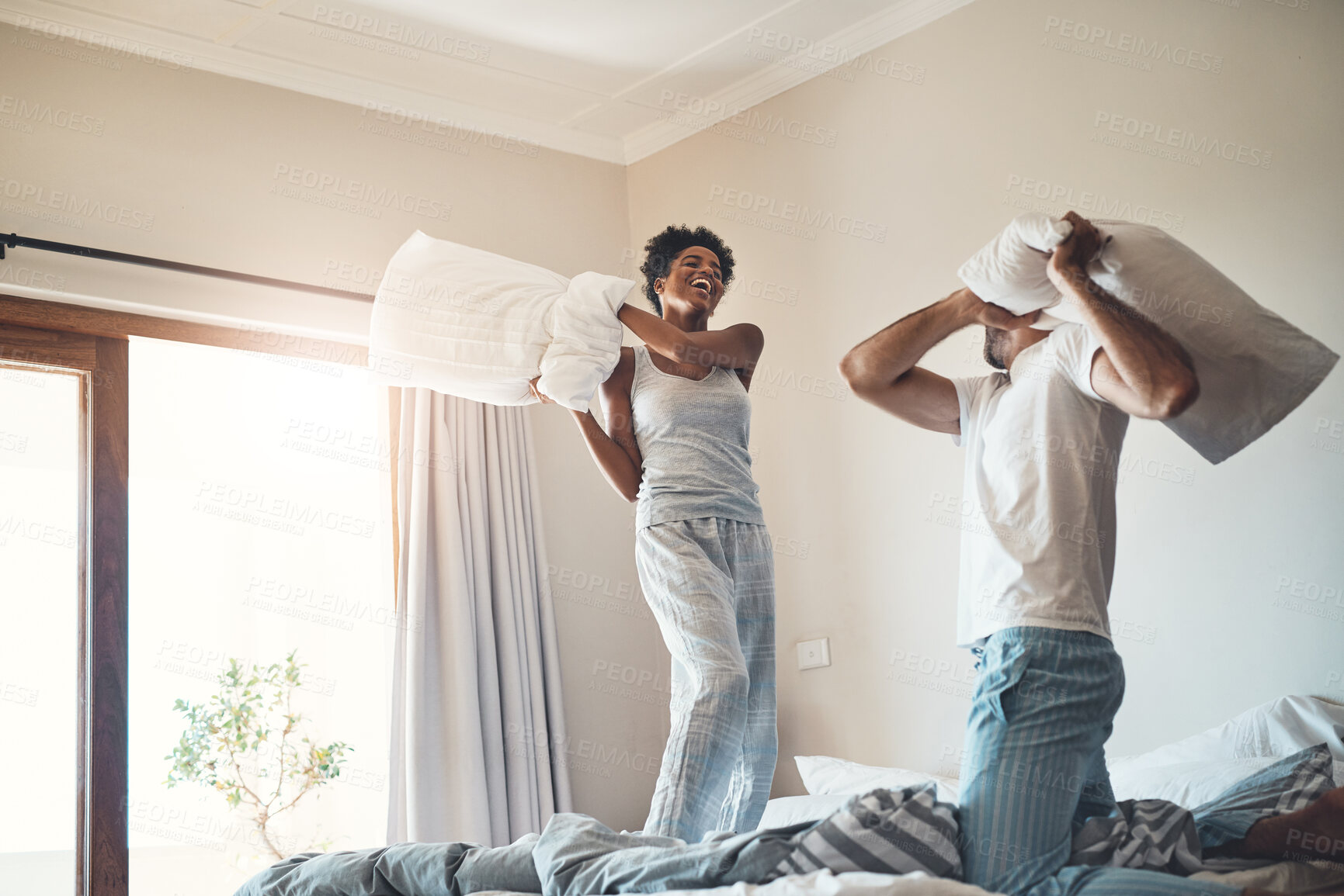 Buy stock photo Happy, fun and playful pillow fight of a loving couple playing in their bedroom at home. Funny male and female laughing, smiling and fighting with pillows in pajamas on the bed in the morning.