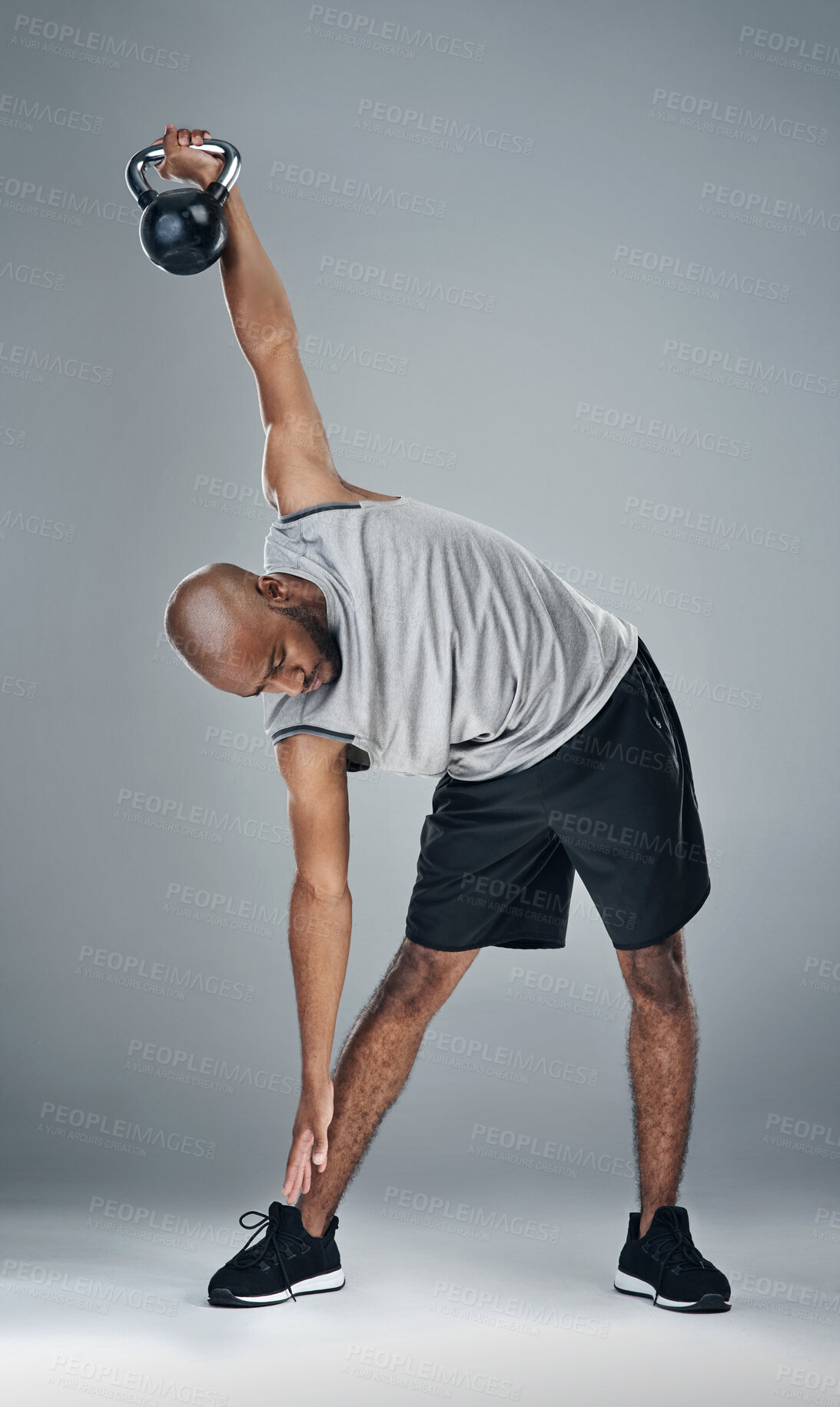 Buy stock photo Stretching, black man and kettle bell in studio for fitness, workout and exercise on gray background. Male person, serious and trainer with sportswear with training for health, wellbeing or self care