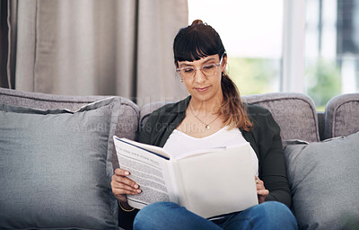 Buy stock photo Cropped shot of an attractive young woman sitting alone in her living room and reading a book