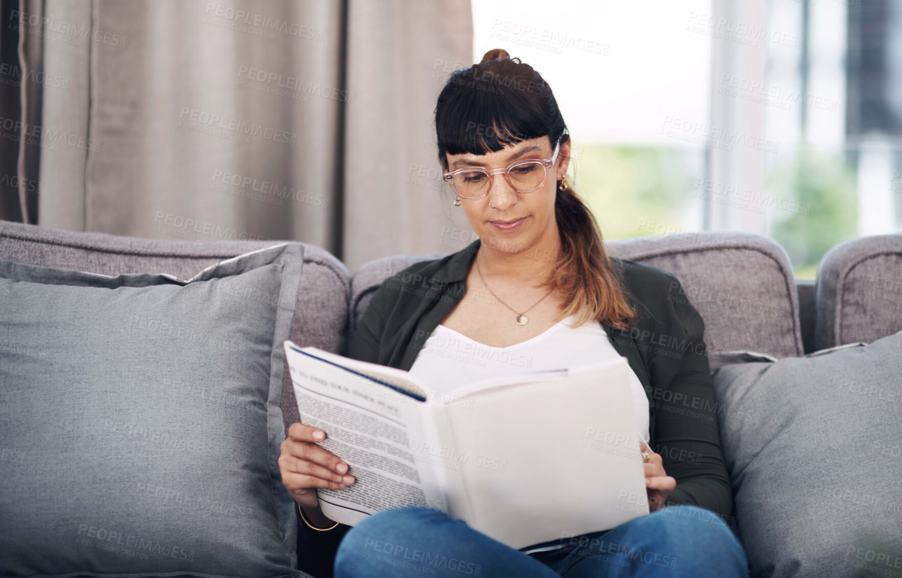 Buy stock photo Cropped shot of an attractive young woman sitting alone in her living room and reading a book