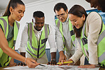 A happy diverse multiracial group of architect colleagues analyzing a blueprint design on a building and discussing plans for the next project. Team of young designers working on a blueprint 