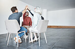 Diverse group of businesspeople giving each other a high five sitting in a meeting in an office at work. Happy women and men joining their hands for motivation while working together