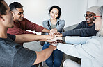 Diverse group of people sitting together in a circle and stacking their hands in the middle after therapy. Smiling support group celebrating after a successful session. Friends support mental health