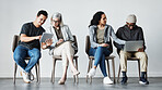 Businesspeople sitting in row using tech devices. Diverse businesspeople waiting for an interview, talking. Group of businesspeople collaborating. Business colleagues sitting in a line, planning