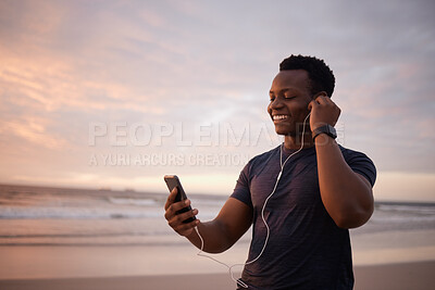 Buy stock photo Phone, earphones and black man at beach with exercise, smile and streaming music at sunset. Ocean, fitness and happy runner with smartphone for video call, workout schedule or podcast on mobile app.