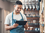 Shot of one young hispanic waiter using a digital tablet device while working in a store or cafe. Happy man checking inventory and stock of products while planning and browsing online