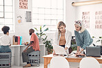 Two focused caucasian businesswomen talking and looking at a document together at work. Female businesspeople having a meeting at a table together. Businesspeople planning and discussing a strategy