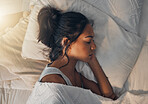 A beautiful young mixed race woman sleeping in a soft comfortable bed at home. One hispanic female feeling exhausted and resting in a comforting bed