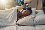 A beautiful young mixed race woman sleeping in a soft comfortable bed at home. One hispanic female feeling exhausted and resting in a comforting bed