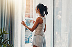 A beautiful young Hispanic woman enjoying a warm cup of coffee for breakfast. One mixed race female drinking tea while looking at the view from a window in her apartment