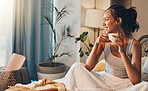 A beautiful young Hispanic woman enjoying a warm cup of coffee for breakfast. One mixed race female drinking tea while sitting in bed and daydreaming