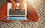 Above view of unknown mixed race woman using laptop for blogging in home living room. Hispanic entrepreneur sitting cross legged alone on lounge floor and typing blog post on technology. Remote worker