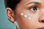 An attractive young mixed race woman posing with cream moisturiser on her face against a green studio background. Beautiful hispanic using a skin products to keep her face clean and healthy