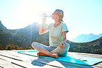 Senior woman sitting on her yoga mat in nature and drinking water. Living active and healthy lifestyle