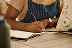 Closeup on hands of african american designer. Tailor writing in her notebook. Creative designer writing a list in a notebook. Professional entrepreneur planning in her creative studio.
