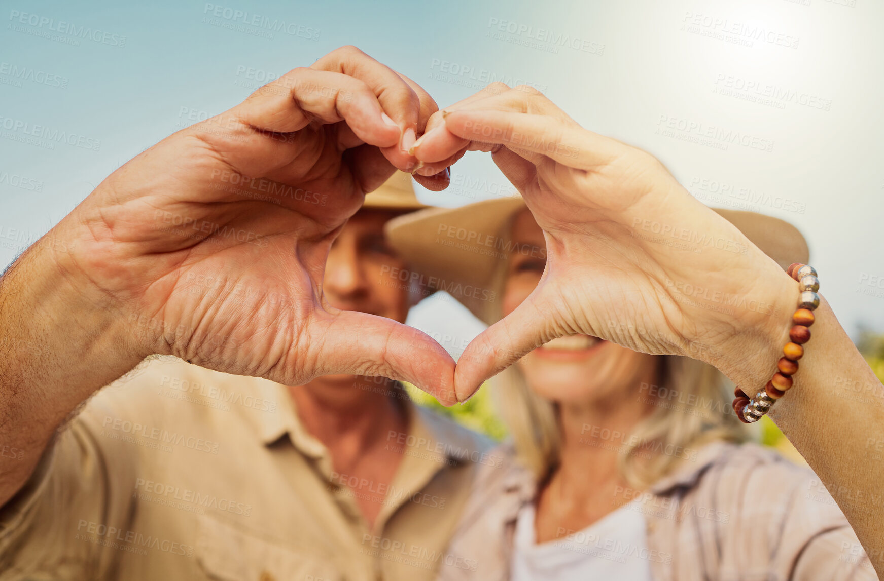 Buy stock photo Couple, happy and love sign by nature for relationship, holiday and bonding together on date with hug. Mature, people and heart hands countryside farm for romance, vacation and embrace with sunshine