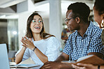 Three young happy businesspeople having a meeting while sitting at a table and working on a laptop at work. Business professionals talking and planning in an office together. Hispanic woman discussing a business strategy with coworkers