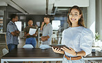 Portrait of a happy mixed race businesswoman working on a digital tablet in an office. Cheerful hispanic female businessperson wearing glasses holding and using social media on a digital tablet at work