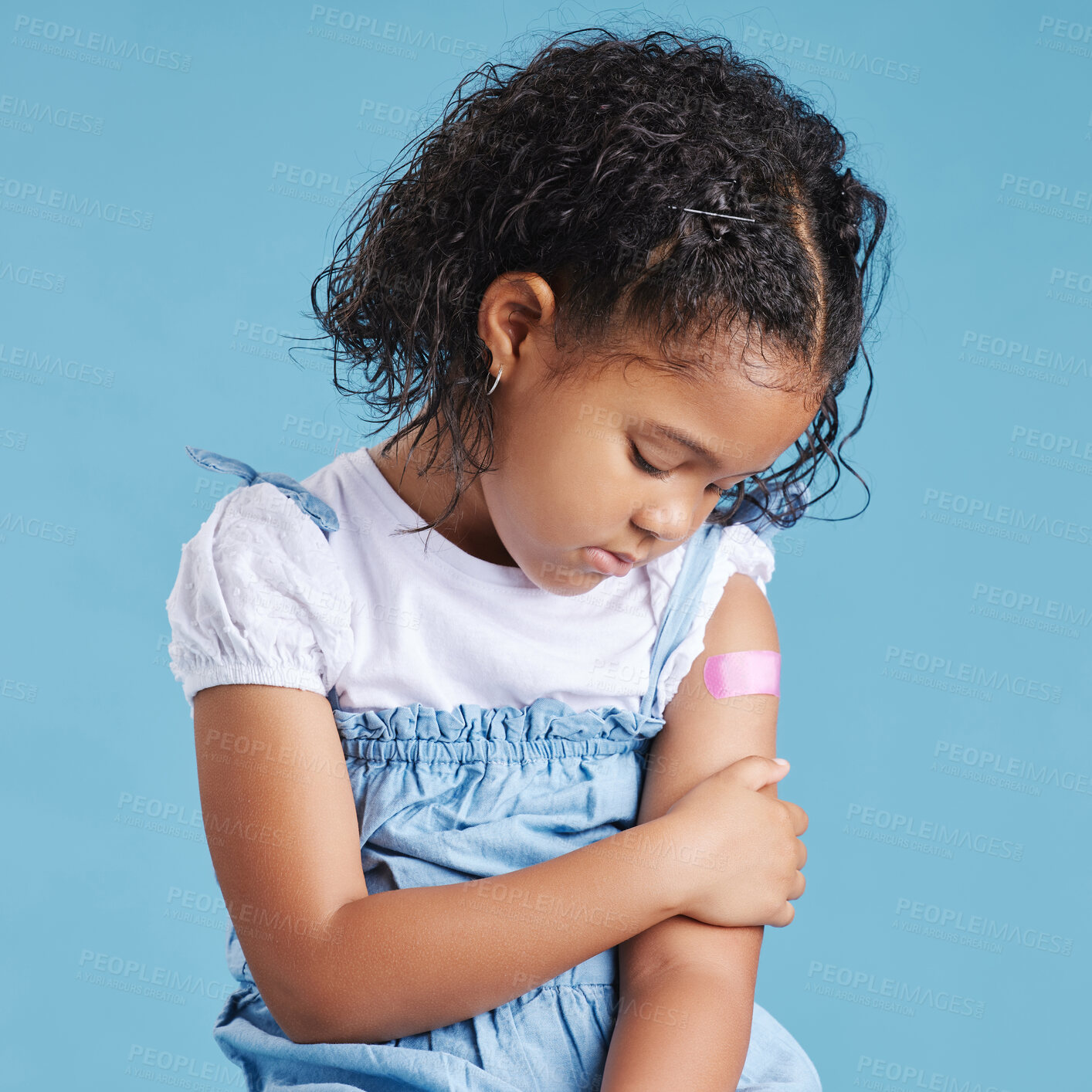 Buy stock photo Sad, plaster and kid in studio for injection, vaccine or medical booster shot for health. Emotions, healthcare and girl kid with bandage on arm for immunization, hurt or injury by blue background.
