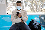 Black businessman travelling alone. A young african american businessman using a cellphone while sitting at the window on a train during his commute to the city