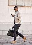 Black businessman travelling alone.A african american businessman walking around town with his luggage while looking at his smartphone and smiling in the city