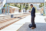 Black businessman travelling alone. A young african american businessman waiting for a train at a railway station and using his wireless cellphone during his commute at a train station