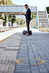 Black businessman travelling alone. A young african american businessman waiting for a train at a railway station and using his wireless cellphone during his commute at a train station