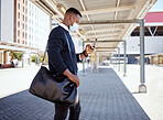 Black businessman travelling alone. A young african american businessman waiting for a train at a railway station and using his wireless cellphone during his commute at a train station