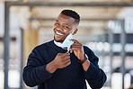 Portrait of a young businessman standing in the street in the city smiling and looking happy on a sunny day. African american male expressing happiness on his face