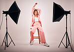 Portrait of a young mixed race female posing in trendy fashionable clothing while chilling on a chair in a studio shoot. Hispanic woman showing the latest fashion collection with a cool style and pose