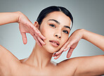 Portrait of a beautiful mixed race woman touching smooth soft skin in a studio. Hispanic model with healthy natural glowing skin looking confident against grey copyspace while doing routine skincare