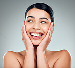 A beautiful young mixed race woman with glowing skin posing against grey copyspace background. Hispanic woman with natural looking eyelash extensions smiling while feeling her smooth skin in a studio