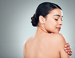 A beautiful young mixed race woman with glowing skin posing against grey copyspace background. Hispanic woman with natural looking eyelash extensions smiling while feeling her smooth skin in a studio