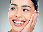 A beautiful young mixed race woman with glowing skin posing against grey copyspace background. Hispanic woman with natural looking eyelash extensions smiling while feeling her smooth skin in a studio